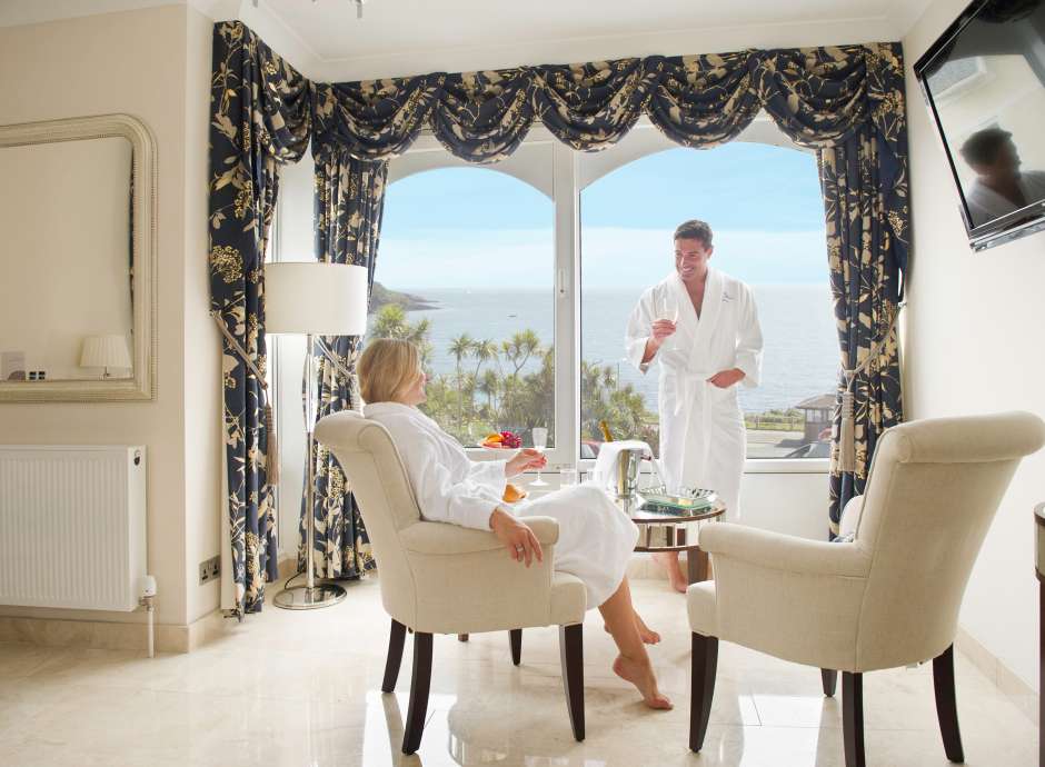 Couple in white robes enjoying stunning sea view from luxury hotel suite 